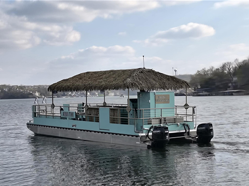 Bombay’s Aqua Tiki Lake Ozark boat on the water with its thatched roof and turquoise hull